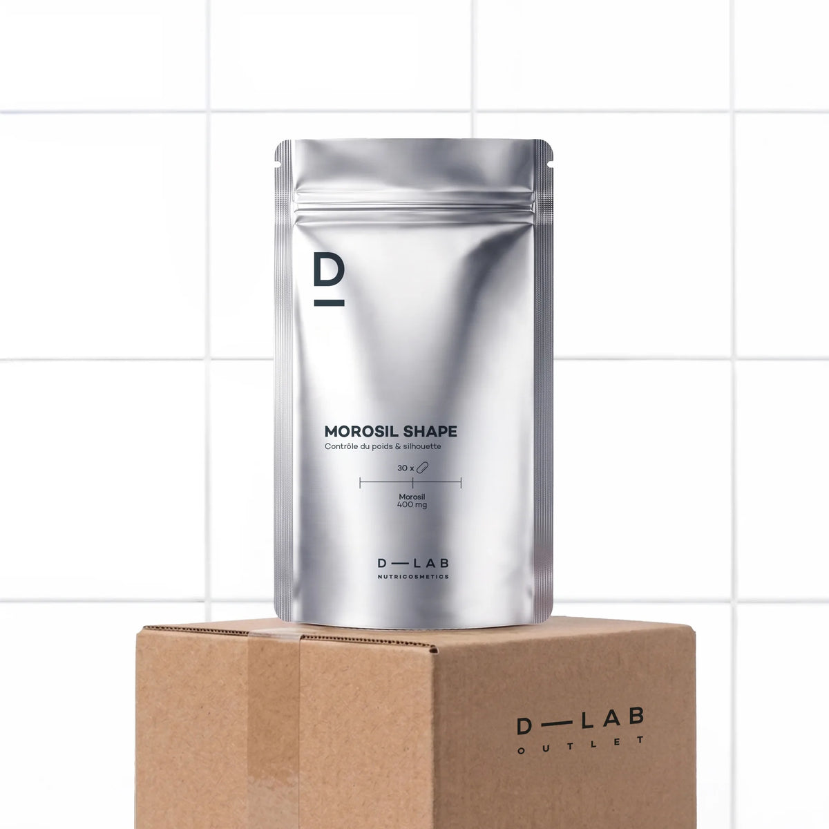 Morosil Minceur Shape D-LAB, doypack, cure d'un mois, sur le carton D-LAB Outlet, devant un mur carrelé blanc